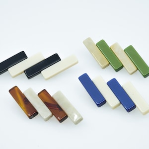 May include: A collection of rectangular, bar-shaped objects in various colors, including black, white, brown, green, and blue. The objects are arranged in diagonal rows against a white background, suggesting a design or craft element.