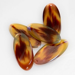 May include: Five oval-shaped, brown and yellow patterned, plastic beads with a hole in the centre.