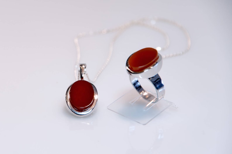 May include: A silver ring and pendant set with oval carnelian stones. The ring has a silver band and the pendant hangs from a silver chain.