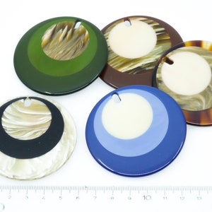 May include: Five round, decorative, colorful, and patterned ornaments with a hole at the top for hanging. The ornaments are made of a hard, glossy material and have a variety of colors and patterns, including green, brown, white, black, and blue.