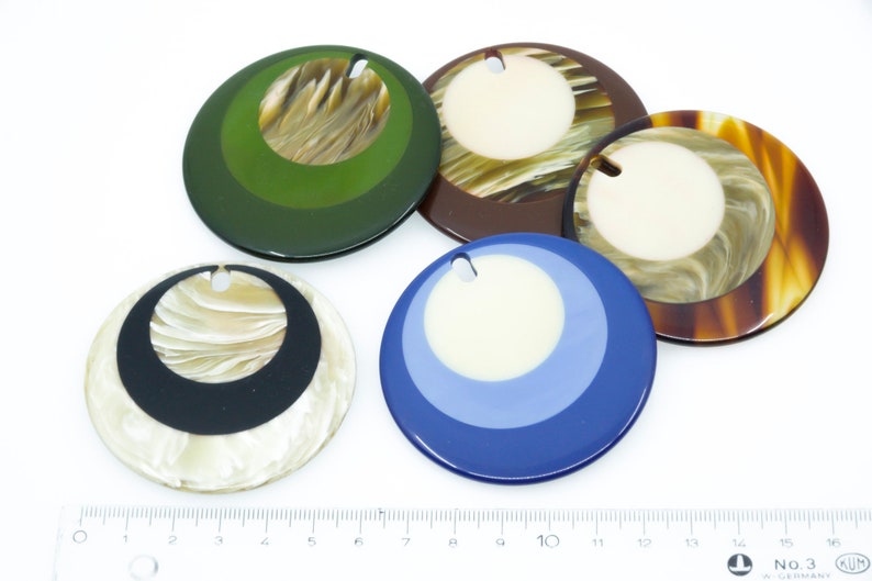May include: Five round, decorative, colorful, and patterned ornaments with a hole at the top for hanging. The ornaments are made of a hard, glossy material and have a variety of colors and patterns, including green, brown, white, black, and blue.