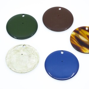 May include: Five round, flat, decorative ornaments with a hole in the center. The ornaments are in various colors, including green, brown, tortoiseshell, cream, and blue.