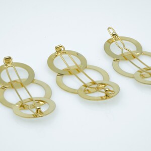 May include: Three gold hair clips with interlocking circles. Each clip has a single bar that runs through the circles.