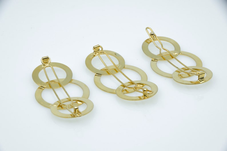 May include: Three gold hair clips with interlocking circles. Each clip has a single bar that runs through the circles.