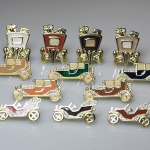 Puede incluir: Nueve broches de coche vintage con detalles en metal dorado y esmalte. Los coches son de varios colores, incluyendo rojo, verde, azul, marrón y negro. Cada coche tiene un techo blanco, crema o marfil.