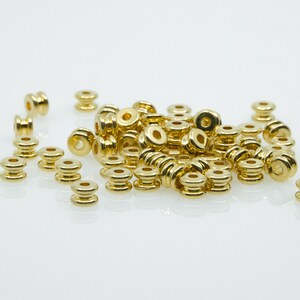 May include: A pile of gold-coloured metal beads, some are stacked on top of each other, and some are scattered around the pile.