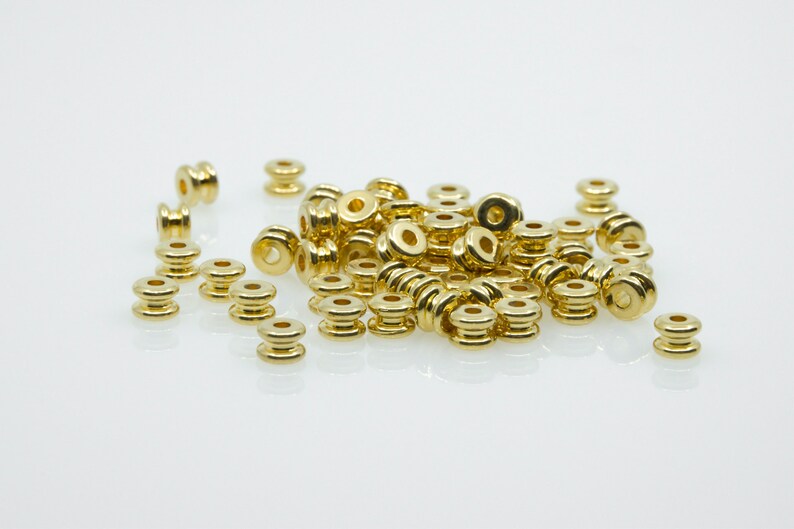 May include: A pile of gold-coloured metal beads, some are stacked on top of each other, and some are scattered around the pile.