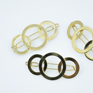 May include: Three gold hair clips with interlocking circles. Each clip has a single bar that runs through the circles.