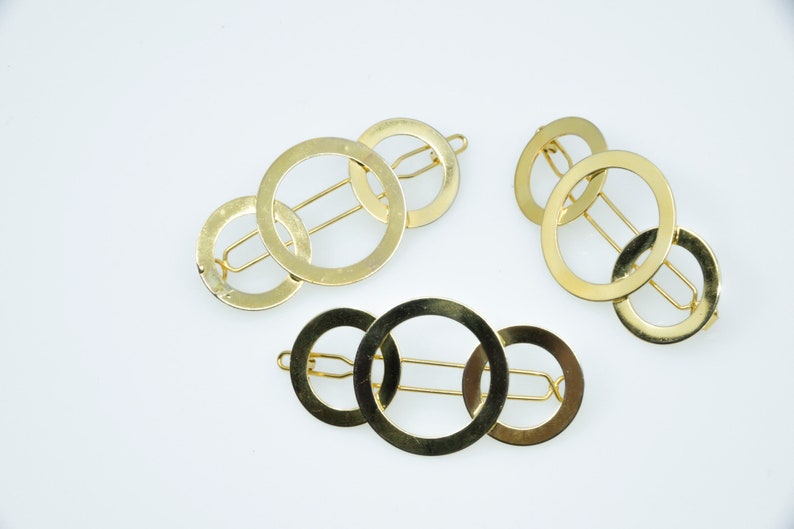 May include: Three gold hair clips with interlocking circles. Each clip has a single bar that runs through the circles.