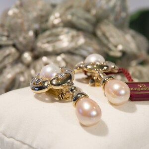 May include: A pair of gold-toned earrings with a pearl accent. The earrings have a floral design with a large, round pearl at the top and a teardrop-shaped pearl hanging below. A red tag is attached.