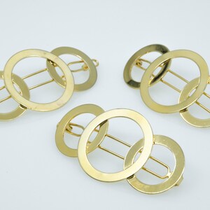 May include: Three gold metal hair clips with interlocking circles. Each clip has a bar in the centre for holding hair.