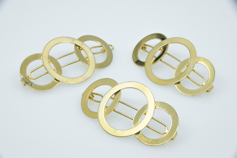 May include: Three gold metal hair clips with interlocking circles. Each clip has a bar in the centre for holding hair.