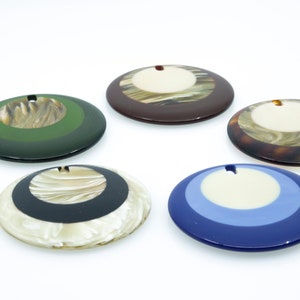 May include: Five round, decorative, multi-colored, resin ornaments with a hole in the center. The ornaments have a white center circle surrounded by concentric circles of different colors.