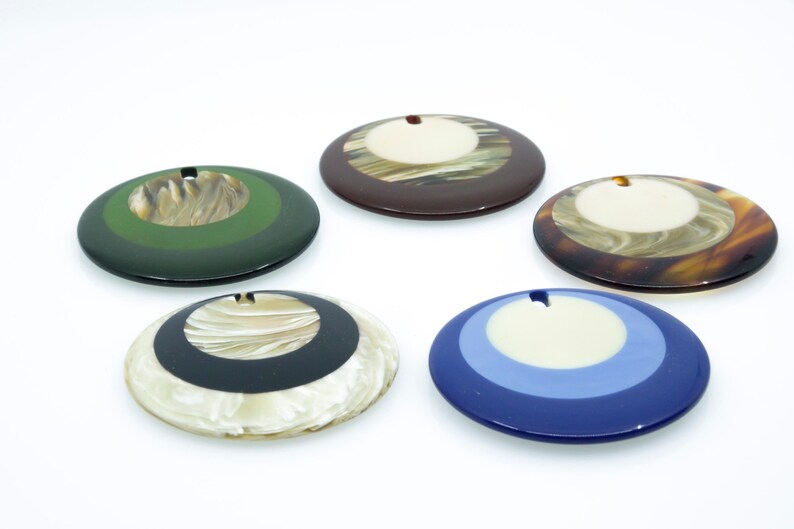 May include: Five round, decorative, multi-colored, resin ornaments with a hole in the center. The ornaments have a white center circle surrounded by concentric circles of different colors.