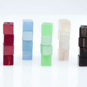 May include: Five stacks of square beads in various colours: red, light blue, green, off-white, and black. Each stack is composed of four beads. The beads have a glossy finish and are arranged vertically, creating a visually appealing display.