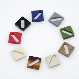 Może przedstawiać: Zestaw ośmiu kwadratowych plastikowych klamer z prostokątnym otworem w środku. Klamry są w różnych kolorach, w tym czarny, czerwony, niebieski, szary, zielony, beżowy, brązowy i biały.