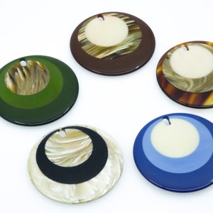 May include: Five round, decorative, resin pendants with a hole at the top for hanging. The pendants are layered with different colors and patterns, including brown, green, blue, black, and white.