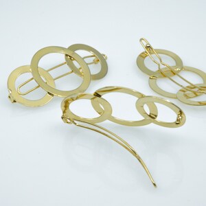 May include: Two gold hair clips. One clip is made of three interlocking circles. The other clip is made of five interlocking ovals.