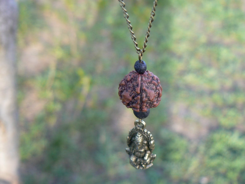 Puede incluir: Un collar marr&oacute;n y negro con un peque&ntilde;o colgante dorado detallado. El colgante es una representaci&oacute;n de una figura sentada. El collar est&aacute; hecho de una cadena con cuentas negras.