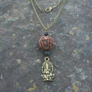 Puede incluir: Un collar de cadena dorada con una cuenta de piedra de lava marr&oacute;n y negra y un colgante dorado con una deidad sentada.