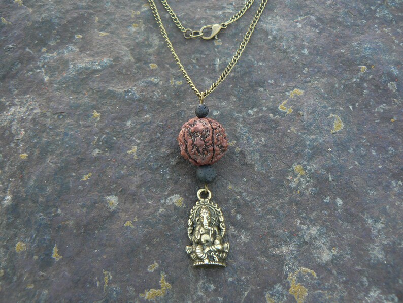Puede incluir: Un collar de cadena dorada con una cuenta de piedra de lava marr&oacute;n y negra y un colgante dorado con una deidad sentada.