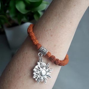 May include: A brown beaded bracelet with a silver sun charm. The bracelet is made of small, round beads and has a simple design.