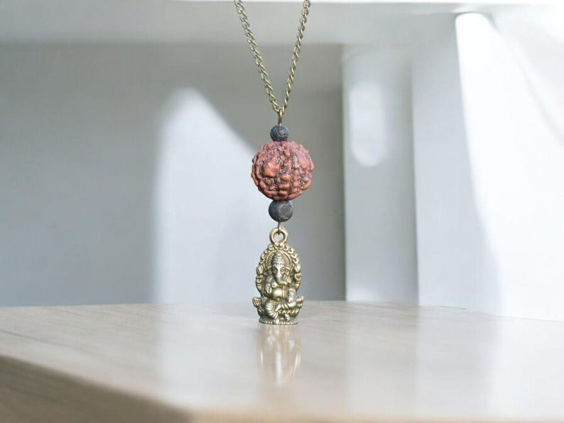 Puede incluir: Un collar de oro con una cuenta marr&oacute;n y negra y un peque&ntilde;o colgante de oro de la deidad hind&uacute; Ganesha.
