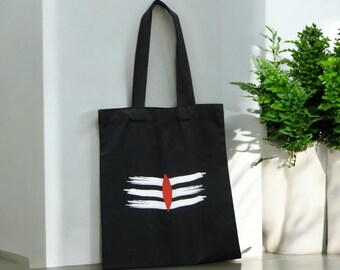 May include: A black tote bag with a white and red symbol printed on the front. The symbol is a stylized representation of the Hindu god Shiva's third eye.