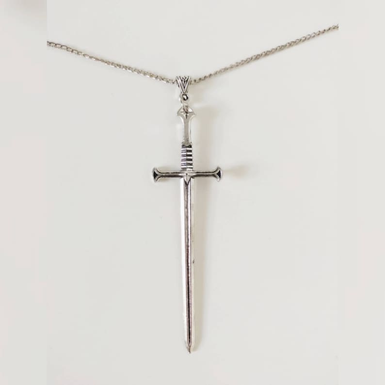 Op de afbeelding: Een zilveren zwaard ketting met een hanger. Het zwaard heeft een gedetailleerd ontwerp en een puntige punt.
