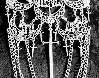 May include: A silver necklace with a large, ornate pendant featuring a sword design. The pendant is surrounded by smaller, crescent-shaped charms and hangs from a chain with multiple layers.