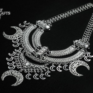 Peut inclure: Un collier en argent avec un design en couches comprenant des breloques en forme de croissant de lune et des détails complexes. Le collier est de style chaîne et est orné de perles décoratives.