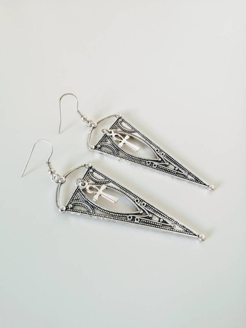 May include: Silver dangle earrings with a triangle shape and an ankh charm.