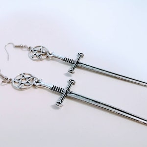 May include: A pair of silver earrings featuring a sword design with a pentagram charm at the top.