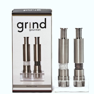 Puede incluir: Un juego de dos molinillos de sal y pimienta plateados con recipientes de acrílico transparente. Los molinillos están etiquetados como "Reflex II Set" y están empaquetados en una caja con el logotipo "grind gourmet".