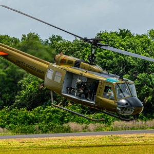 Puede incluir: Un helicóptero militar verde con las palabras "United States Army" en el lateral despega de una pista de hierba.