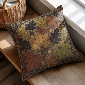 Peut inclure: Un coussin carré arborant un motif imprimé de feuilles d'automne dans des tons orange, jaune, marron et vert foncé, agrémenté de petits glands. Le motif est encadré par une bordure marron foncé avec des volutes décoratives.