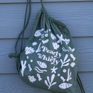 May include: A green drawstring bag with white illustrations of sea life and the text "Pearly Whirly".