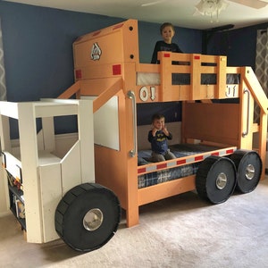 May include: A wooden bunk bed shaped like a garbage truck. The top bunk has a white railing and the bottom bunk has a blue and white patterned mattress. Two children are sitting on the beds. The truck is painted orange and white.