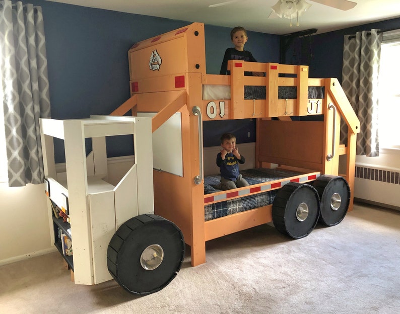 May include: A wooden bunk bed shaped like a garbage truck. The top bunk has a white railing and the bottom bunk has a blue and white patterned mattress. Two children are sitting on the beds. The truck is painted orange and white.