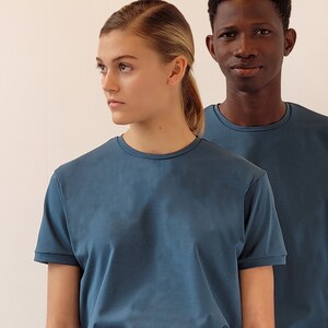 Op de afbeelding: Twee mensen dragen blauwe T-shirts. De persoon links is een vrouw met blond haar en de persoon rechts is een man met kort zwart haar.