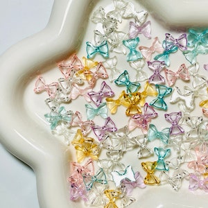 May include: A collection of pastel-colored plastic bows with silver glitter accents. The bows are scattered on a white star-shaped dish.
