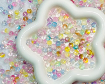 May include: A white ceramic star-shaped dish filled with iridescent glass beads in various pastel colors, including pink, blue, yellow, and clear.