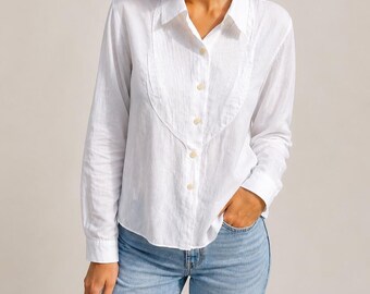 May include: White long-sleeve shirt with a unique, ruffled bib detail. The shirt features a classic collar and button-down front. The model is wearing light blue jeans. This shirt is a versatile addition to any wardrobe.