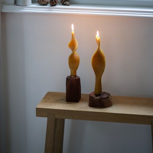 Può includere: Due candele gialle a spirale accese su portacandele in legno, su un tavolo in legno chiaro.