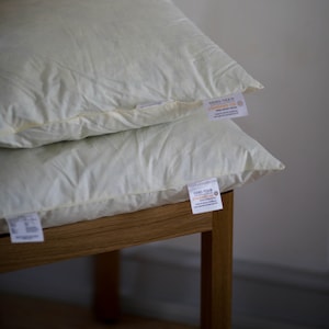 Pode incluir: Duas almofadas brancas com uma etiqueta branca que diz "Oeko-Tex Standard 100" na almofada de baixo. As almofadas estão sobre uma estrutura de cama de madeira.