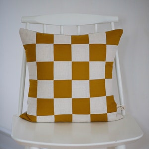 Könnte beinhalten: Ein weißer Stuhl mit einem gelben und weißen karierten Kissen. Das Kissen hat ein kleines Etikett mit der Aufschrift "Min."