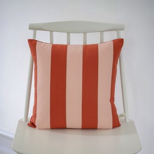 Könnte beinhalten: Ein weißer Stuhl mit einem rot-weiß gestreiften Kissen. Das Kissen hat ein kleines Etikett mit der Aufschrift "cotton".