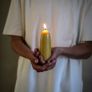 Può includere: Una persona tiene in mano una candela di cera d'api gialla accesa.