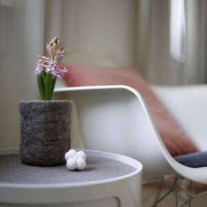 May include: A white side table with a gray top and a gray felt planter with a pink flower inside. A white decorative flower sits on the table top.