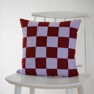 Könnte beinhalten: Ein weißer Stuhl mit einem rot-violetten karierten Kissen. Das Kissen hat ein kleines Etikett mit der Aufschrift "Otten".